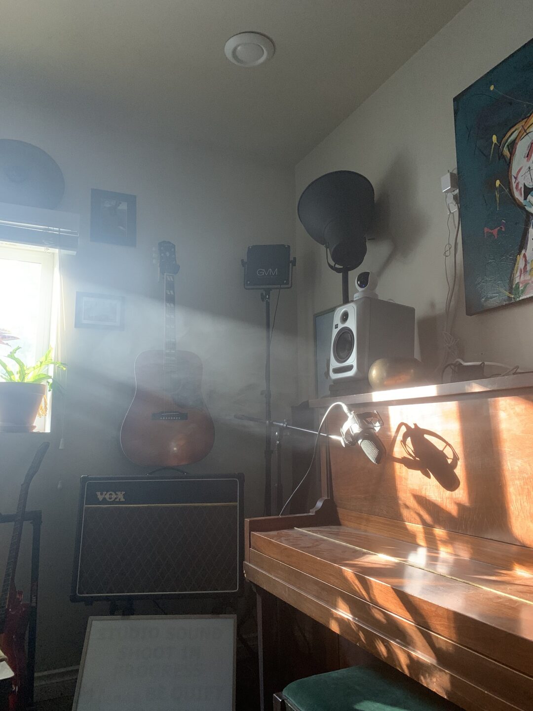 A piano with a mic in front of it, and a sunbeam falling so that the shadow of the microphone falls on the face of the piano