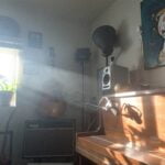 A piano with a mic in front of it, and a sunbeam falling so that the shadow of the microphone falls on the face of the piano