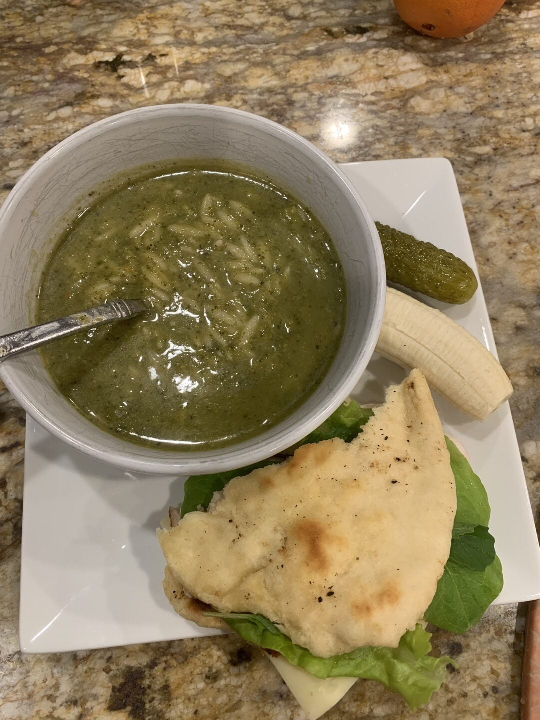 A bowl of homemade broccoli soup accompanied by other lunch items on the counter.