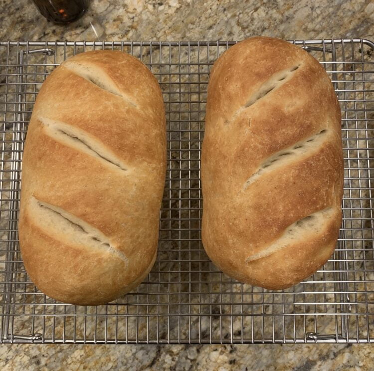 Two fresh loaves of French bread resting on a wire cooling rack.