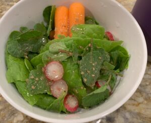 A bowl of salad with fresh greens, baby carrots, and radish slices.