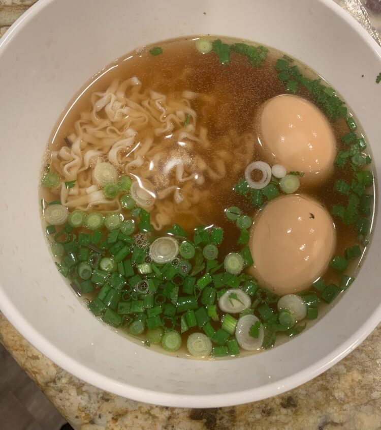 A white bowl filled with ramen noodles, broth, soft boiled eggs and green onions.