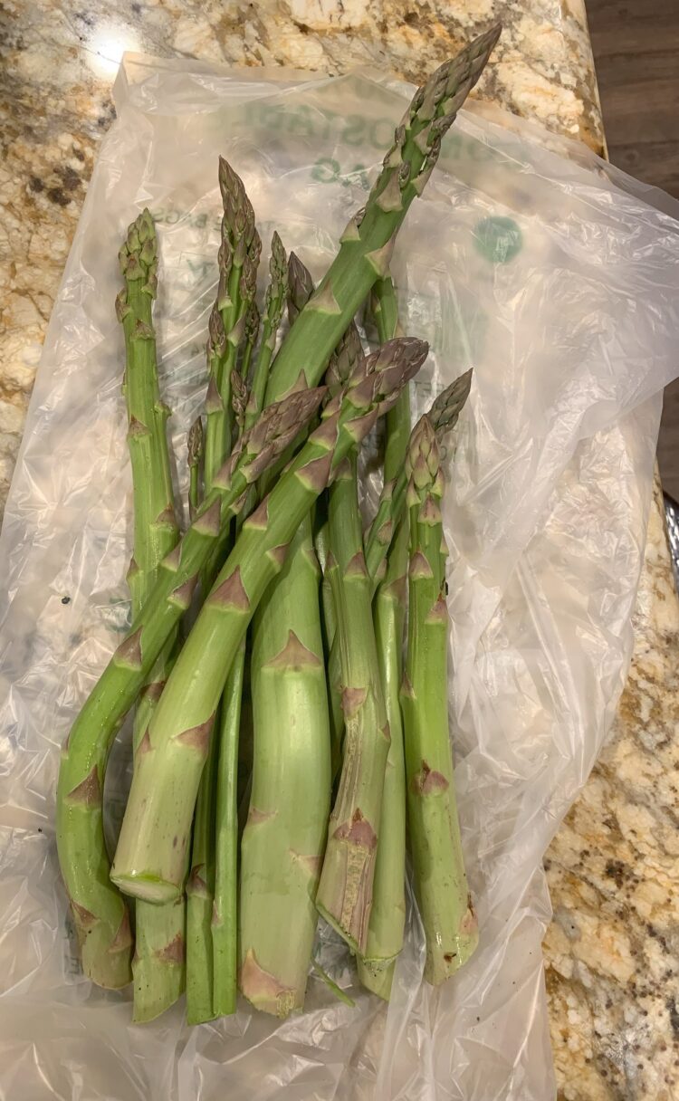 A bundle of freshly picked asparagus spears lying on a marble countertop.