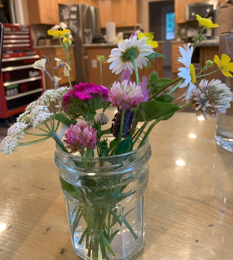 A glass mason jar filled with a bouquet of colorful wildflowers.