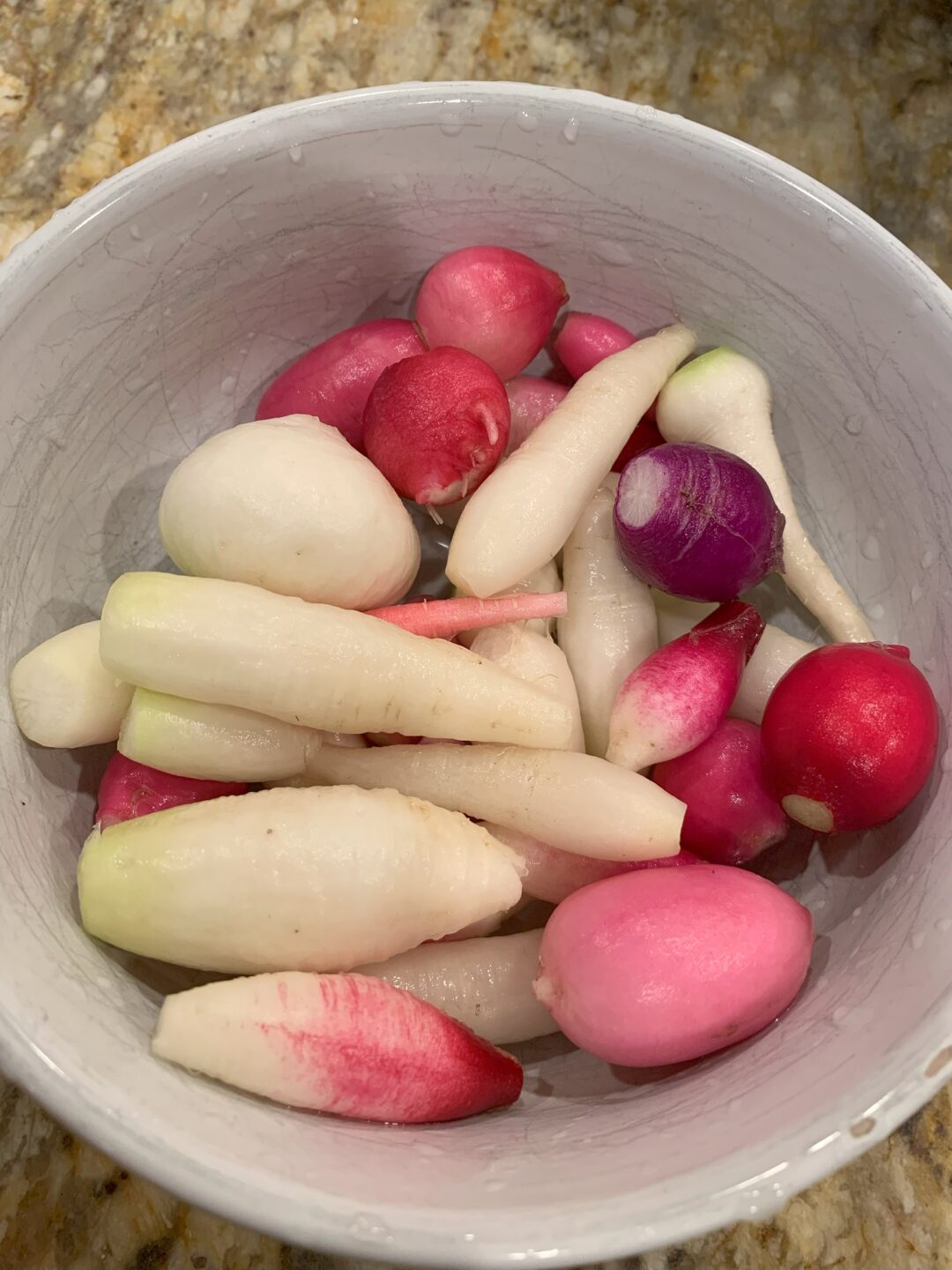 A white bowl full of freshly picked radishes.