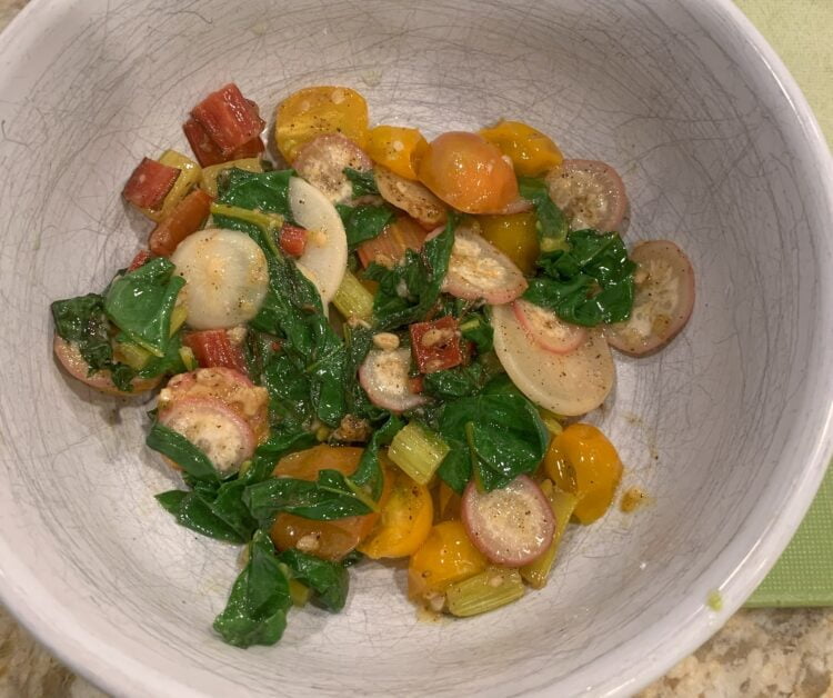 A white bowl filled with scrambled eggs, cherry tomatoes, radishes and Swiss chard.