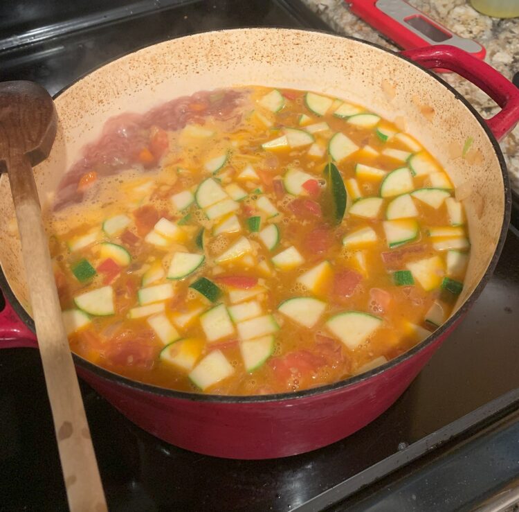 A large, red Dutch oven pot filled with simmering zucchini meatball soup.