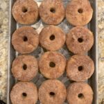 A pan full of a dozen fresh, sugary donuts.